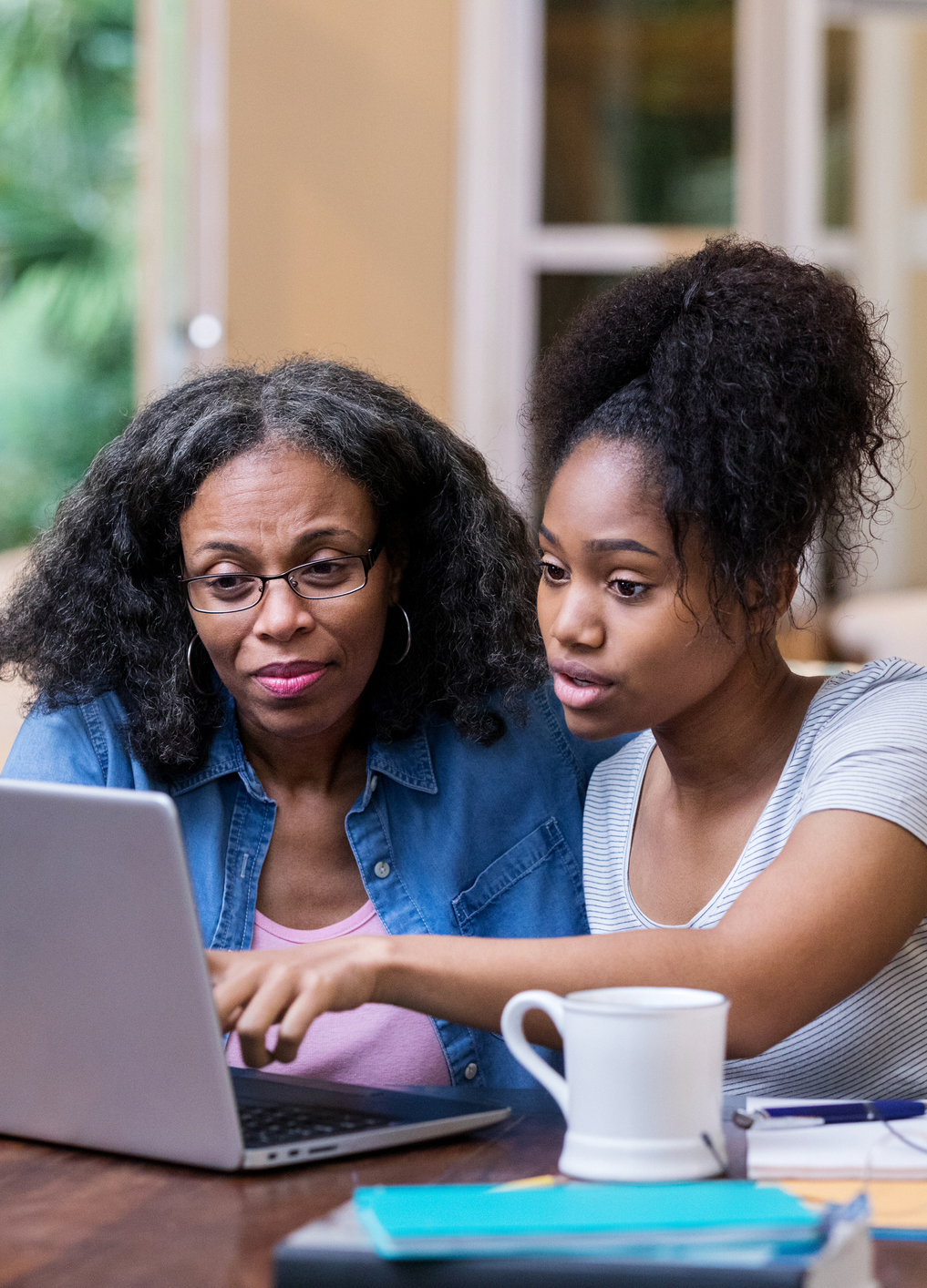 Young woman and her mature mom look at something on a laptop as the young woman studies for a college exam.