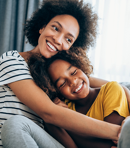 Lovely mother embracing her cute daughter on the sofa at home.